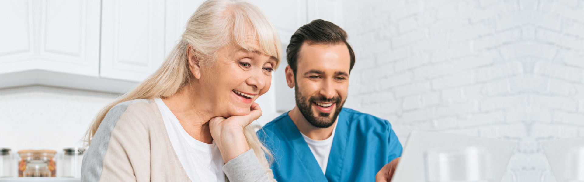 smiling young caregiver and happy senior woman using laptop together
