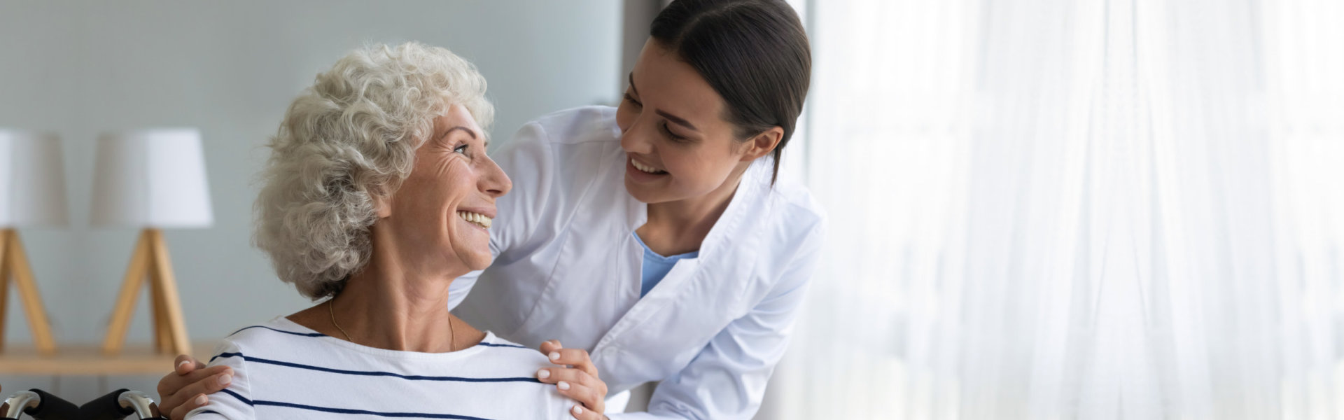 Smiling caregiver caring about happy handicapped senior woman in wheelchair