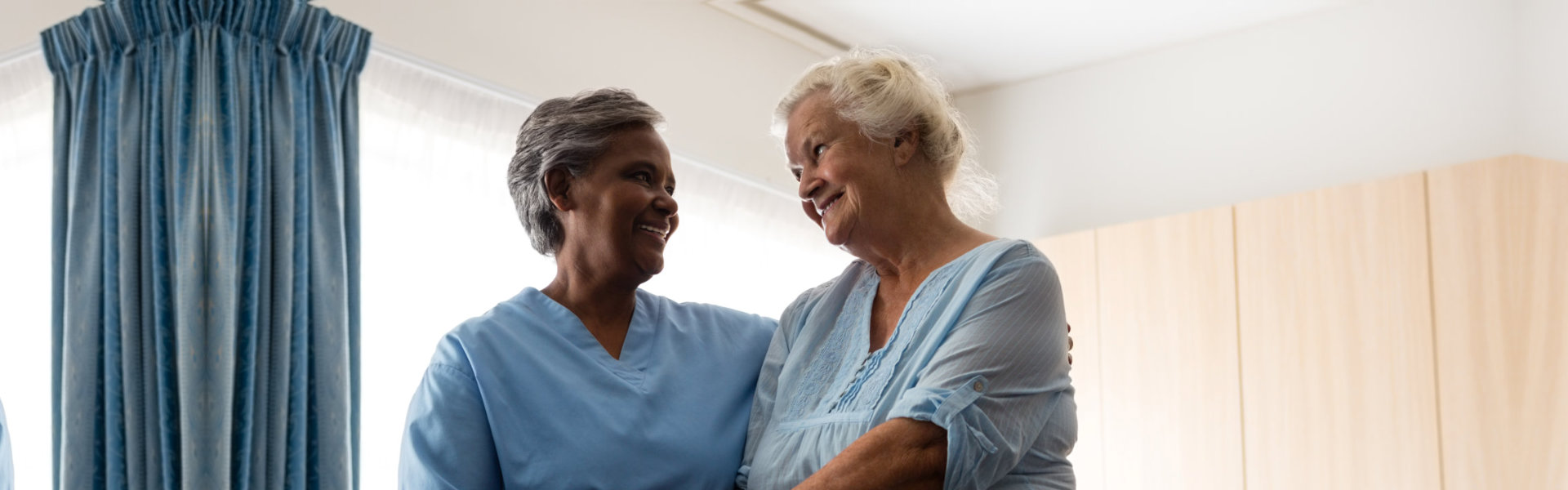 Nurse assisting senior patient in walking with walker at nursing home